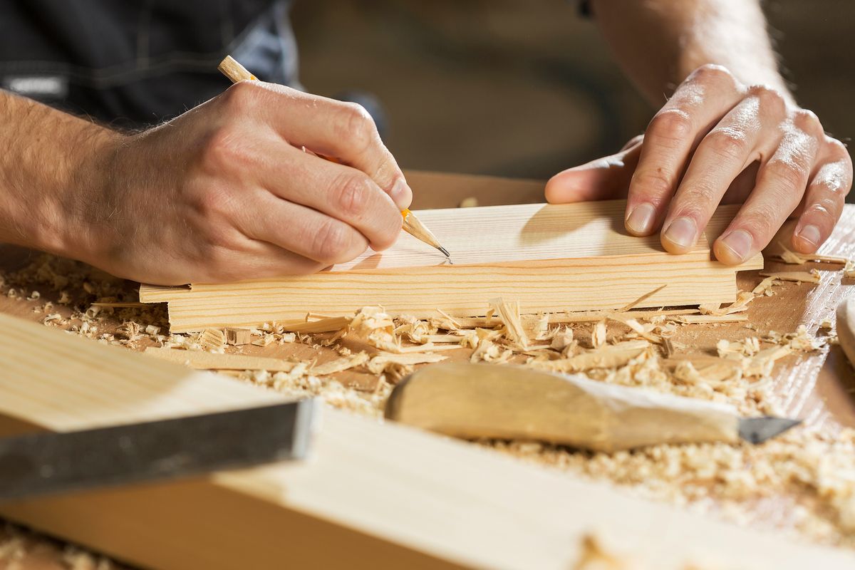 Handen die met een potlood een lijn op een houten plank tekenen, tussen houtkrullen