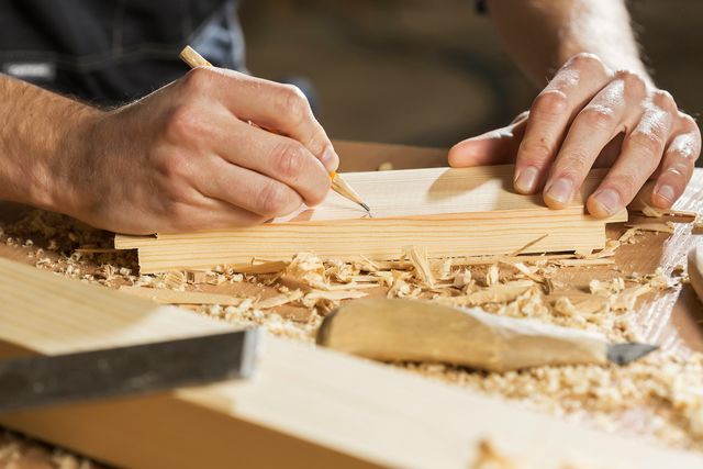 Handen die met een potlood een lijn op een houten plank tekenen, tussen houtkrullen